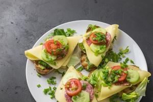 Frühlingsgesunde Sandwiches mit Käse, Salat und Tomaten bestreut mit Schnittlauch auf Tellern auf dunklem Hintergrund foto