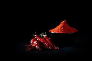 Chilipulver in schwarzer Schale mit roten, getrockneten Chilis auf schwarzem Hintergrund foto