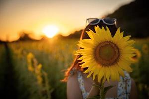 Fröhliches, fröhliches asiatisches Mädchen mit Sonnenblume, das die Natur genießt und im Sommer im Sonnenblumenfeld lächelt. foto