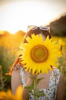 Fröhliches, fröhliches asiatisches Mädchen mit Sonnenblume, das die Natur genießt und im Sommer im Sonnenblumenfeld lächelt. foto