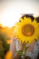 Fröhliches, fröhliches asiatisches Mädchen mit Sonnenblume, das die Natur genießt und im Sommer im Sonnenblumenfeld lächelt. foto