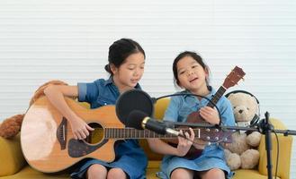 ältere und jüngere Schwestern singen ein Lied, während sie zusammen Gitarre und Ukulele spielen