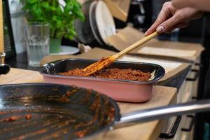 Lasagne zubereiten. eine Person, die Schichten mit Tomatensauce mit Fleisch ausbreitet.