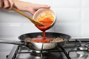 die Person, die Tomatensauce über Rindfleisch gießt. Zubereitung eines italienischen Gerichtes. foto