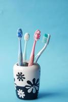 bunte Zahnbürsten in weißer Tasse vor blauem Hintergrund