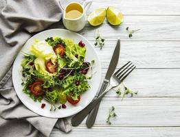 frische grüne gemischte Salatschüssel mit Tomaten und Microgreens auf weißem Holzhintergrund. gesundes Essen, Ansicht von oben. foto