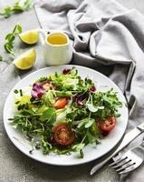 frische grüne gemischte salatschüssel mit tomaten und microgreens auf konkretem hintergrund. gesundes Essen, Ansicht von oben. foto
