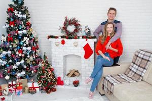 junges Paar zu Hause mit Kamin und Weihnachtsbaum. Weihnachtsinterieur foto