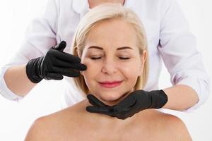 Kosmetikerin untersucht das Gesicht einer Frau mit Altersfalten - Alterungs- und Hautpflegekonzept foto