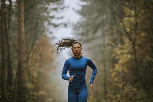 junge Frau, die im Herbst auf dem Waldweg in Richtung Kamera läuft foto