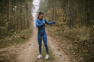 junge Frau im blauen Trainingsanzug, die sich vor dem Training im Herbstwald ausdehnt foto