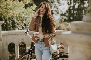 junge Frau mit Handy trinkt Kaffee, um am Herbsttag mit dem Fahrrad zu fahren foto