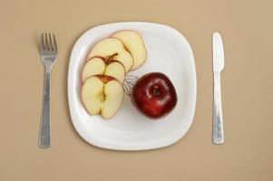 leckerer Apfel und Scheibe in weißem Teller mit Messer und Gabel foto