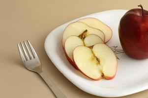 leckerer Apfel und Scheibe in weißem Teller mit Messer und Gabel foto