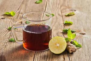 Tasse Tee mit Ingwer, Zitrone und Minze auf Holztisch foto
