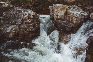 Fluss zwischen Steinen und Felsen. Bach im Steinbett, schneller Gebirgsfluss zwischen Felsen, Wasser kocht in Strömungswirbeln foto