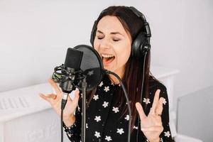 Schöne Frau mit Kopfhörern singt ein Lied in der Nähe eines Mikrofons in einem Tonstudio. Platz für Text oder Werbung foto