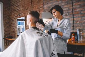 Schöne Frau Friseur macht einen Haarschnitt den Kopf des Kunden mit einem elektrischen Trimmer im Friseurladen. Werbe- und Friseurkonzept. Platz für Text oder Werbung