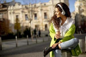 junge Frau hört Musik mit Smartphone auf der Straße und hält Kaffee zum Mitnehmen