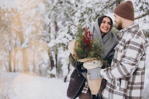 süß jung Paar im Liebe mit Kiefer Strauß Ausgaben Zeit auf Valentinstag Tag im schneebedeckt Winter Wald im Berge foto