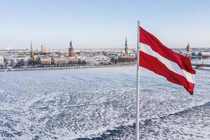 Panorama der Stadt Riga mit einer großen lettischen Flagge im Vordergrund während des sonnigen Wintertages. foto