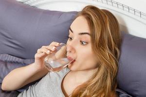 Mädchen trinkt Wasser, das morgens zu Hause im Bett liegt, Gesundheitskonzept foto