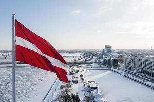 Panorama der Stadt Riga mit einer großen lettischen Flagge im Vordergrund während des sonnigen Wintertages. foto