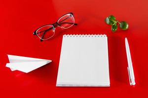 Bürobedarf auf rotem Grund. leeres Notizbuch, Stift und Brille. foto
