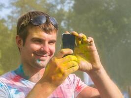 Mann nehmen Foto auf Handy, Mobiltelefon Telefon auf holi Farbe Festival