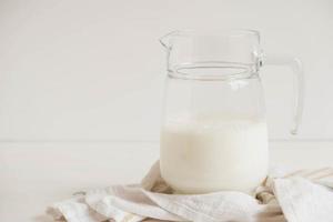 Glaskrug mit Milch und Serviette auf einem weißen Tisch foto