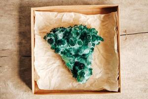 roher Smaragd und Edelstein rauer Bergkristall in einer Kraftpapierbox auf Holzhintergrund foto