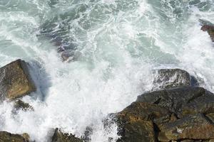 die Wellen brechen an einem steinigen Strand und bilden eine Gischt. Welle und Spritzer am Strand. Wellen, die auf Felsen krachen. foto