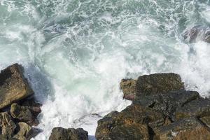 die Wellen brechen an einem steinigen Strand und bilden eine Gischt. Welle und Spritzer am Strand. Wellen, die auf Felsen krachen. foto