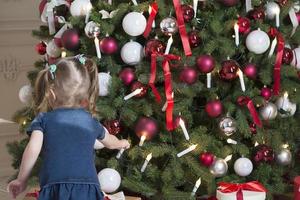 Rückansicht des Kleinkindmädchens, das den Weihnachtsbaum schmückt foto