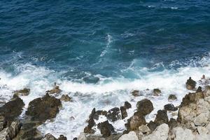 die Wellen brechen an einem steinigen Strand und bilden eine Gischt. Welle und Spritzer am Strand. Wellen, die auf Felsen krachen.