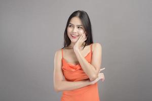 Modeporträt einer schönen Frau, die ein orangefarbenes Kleid trägt, isoliert über grauem Hintergrundstudio