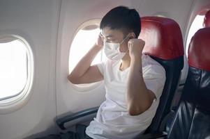 Ein reisender Mann trägt eine Schutzmaske an Bord im Flugzeug, reist unter der Covid-19-Pandemie, Sicherheitsreisen, Protokoll zur sozialen Distanzierung, neues normales Reisekonzept foto