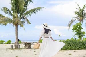 eine glückliche schöne Frau im weißen Kleid, die am Strand, im Sommer und im Ferienkonzept genießt und sich entspannt foto
