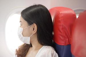 Eine reisende Frau trägt eine Schutzmaske an Bord im Flugzeug, reist unter der Covid-19-Pandemie, Sicherheitsreisen, Protokoll zur sozialen Distanzierung, neues normales Reisekonzept foto
