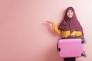 muslimische frau mit hijab hält gepäck auf rosa hintergrund, menschen reisen konzept
