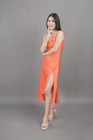 Modeporträt einer schönen Frau, die ein orangefarbenes Kleid trägt, isoliert über grauem Hintergrundstudio