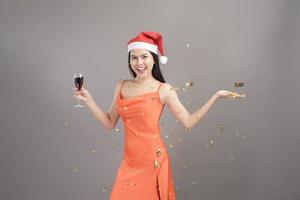 Porträt einer schönen Frau mit rotem Weihnachtsmann-Hut, die Papieraufnahmen feiert und spielt, isoliertes graues Hintergrundstudio, Weihnachten und Neujahrskonzept. foto