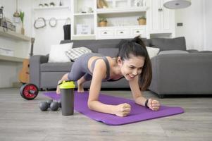 Eine Frau macht Yoga-Plank und sieht sich Online-Trainings-Tutorials auf ihrem Laptop im Wohnzimmer an, Fitness-Workout zu Hause, Gesundheitstechnologiekonzept.