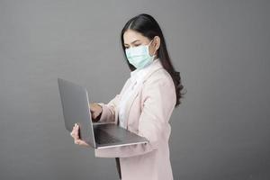 Geschäftsfrau mit Mundschutz hält Laptop-Computer