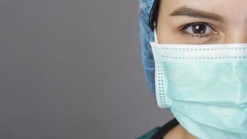 Junge selbstbewusste Ärztin in grünen Peelings trägt eine chirurgische Maske über grauem Hintergrundstudio foto