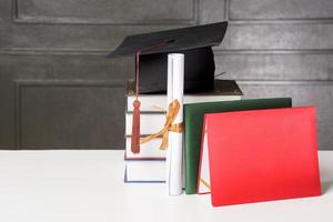 Abschlusskappe mit Büchern auf weißem Schreibtisch, Bildungshintergrund foto