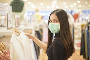 Frau mit Gesichtsmaske kauft Kleidung im Einkaufszentrum