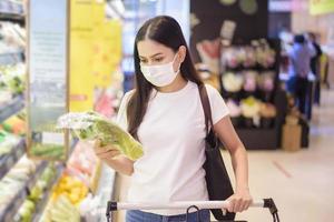 Frau kauft im Supermarkt mit Gesichtsmaske ein