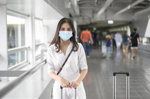Eine reisende Frau trägt eine Schutzmaske auf dem internationalen Flughafen, reist unter der Covid-19-Pandemie, Sicherheitsreisen, Protokoll zur sozialen Distanzierung, neues normales Reisekonzept