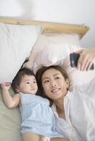 asiatische mutter und ihre kleine tochter machen selfie oder videoanrufe mit vater im bett, familie, heimsicherheit, elternschaft, technologiekonzept foto